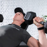 A man lying on a weight bench in a gym, lifting a black 12.5 kg hex dumbbell. do ing bicep curls