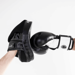 Person wearing a black boxing glove hitting a black boxing pad on a white background