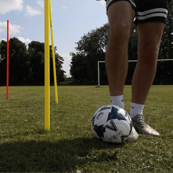 The Hit Sport Training Boundary Poles Orange/Yellow Set stacked in the Ground and a Soccer Player next to it